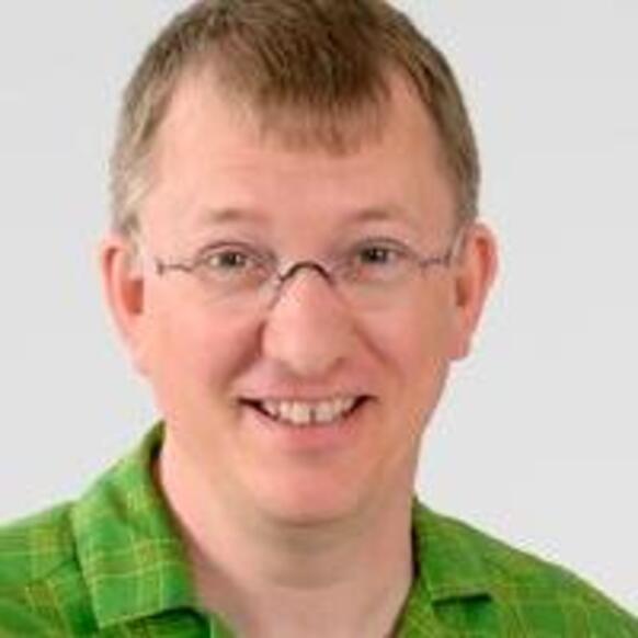 A headshot of Jürgen Hoffmann smiling with glasses wearing a green shirt against a plain background.